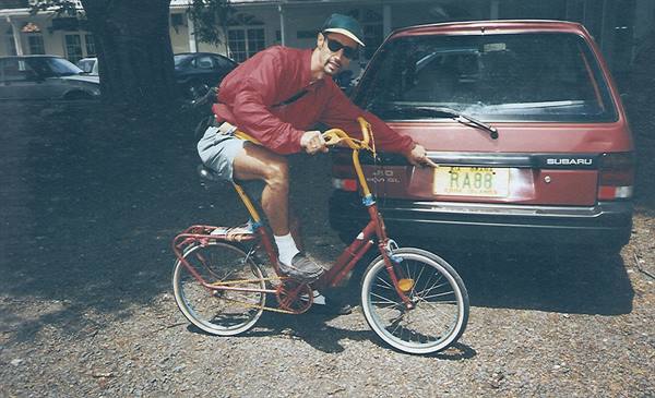 Man in red jacket on a bicycle beside a red Subaru