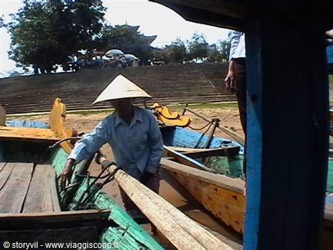 Woman in straw hat among wooden boats on a muddy riverbank