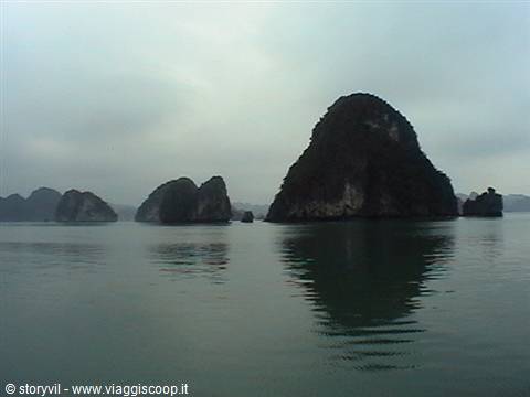 Limestone karst of Ha Long reflected in green water under grey sky
