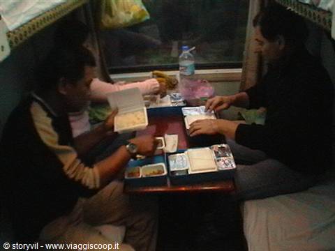 Passengers eating takeout food at the small table in a sleeper train compartment