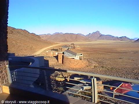 Stone terrace with pool overlooking desert, buildings and mountains under blue sky