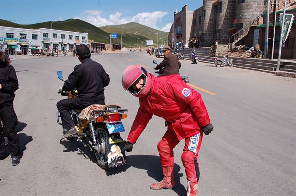 Motorcyclist in red suit chats with a rider on a mountain town square