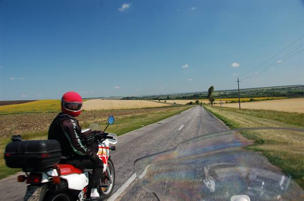 Motorcyclist with red helmet on rural road between cultivated fields