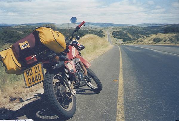 Red motorcycle loaded with yellow bags parked on an asphalt road among hills