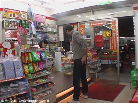 Customer at the counter of a Japanese convenience store, snack shelves and cashier