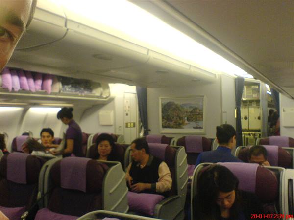 Flight attendant serves passengers in purple aircraft cabin under bright light