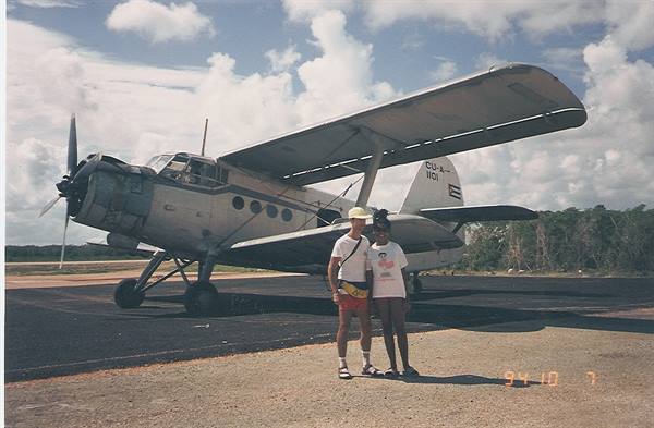 Two tourists beside an Antonov An-2 biplane on a Cuban airfield