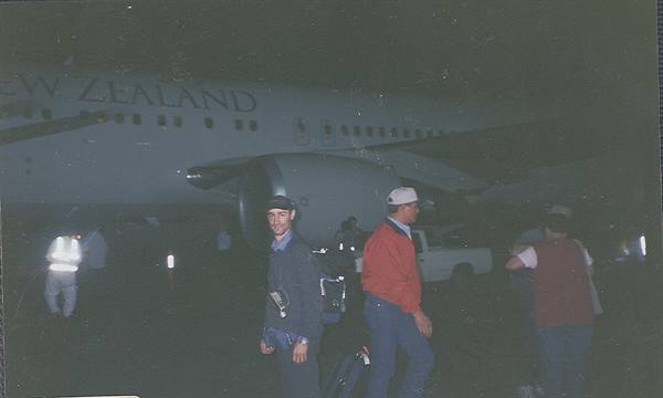 Passengers with luggage descend the stairs of an Air New Zealand plane at night
