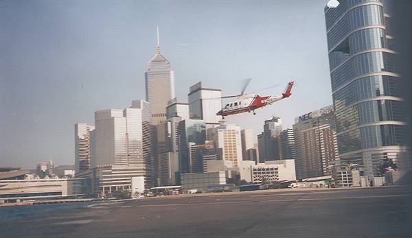 Red and white helicopter takes off from heliport facing Hong Kong skyscrapers