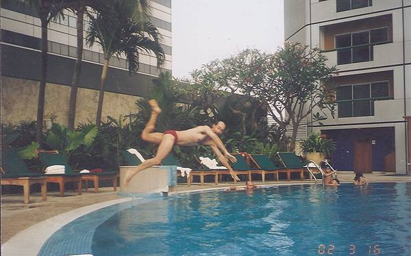 Man diving into a hotel pool surrounded by palms and towers, Singapore