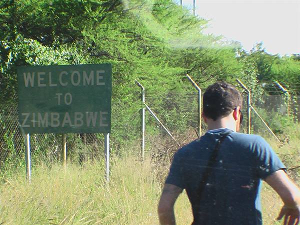 Boy walking past the Welcome to Zimbabwe sign among fences and trees