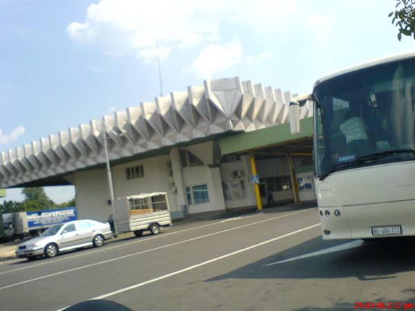 White bus beside a bus station with geometric concrete roof, bright daylight