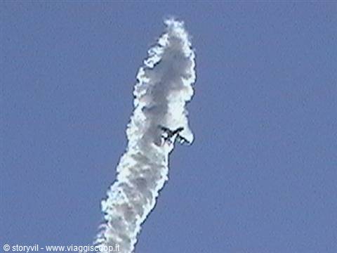 Aerobatic plane streaks through blue sky leaving a long white smoke trail