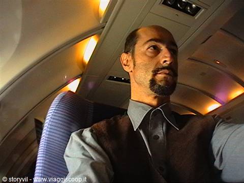 Bearded man seated in an airplane cabin seat, warm cabin lights