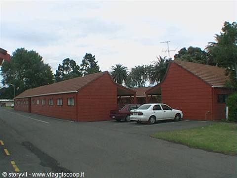 Red-walled motel with sloping roofs, cars parked under a cloudy sky