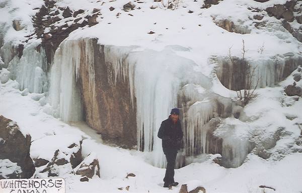 Man standing before frozen waterfall with icicles, Whitehorse sign visible