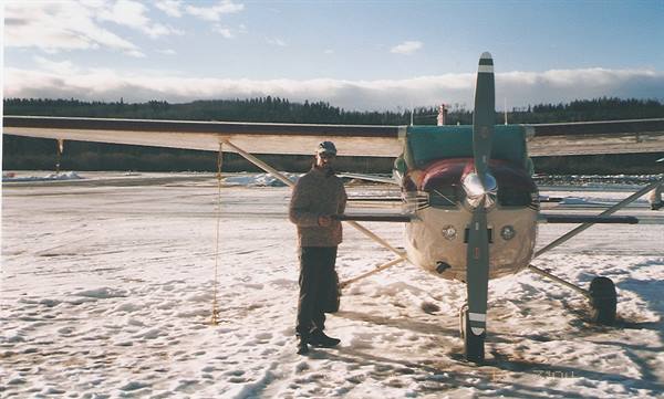 Man beside a propeller plane on a snowy airstrip