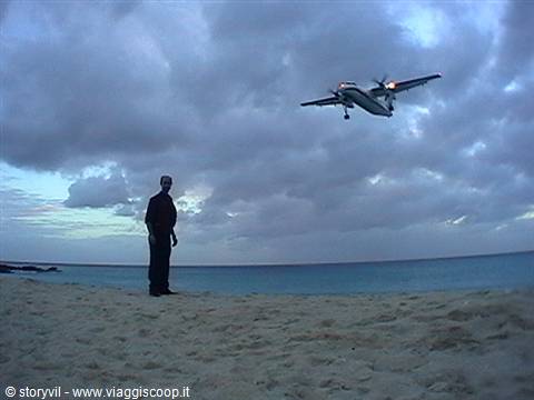 Plane landing low over Maho Beach, man standing on lit sand