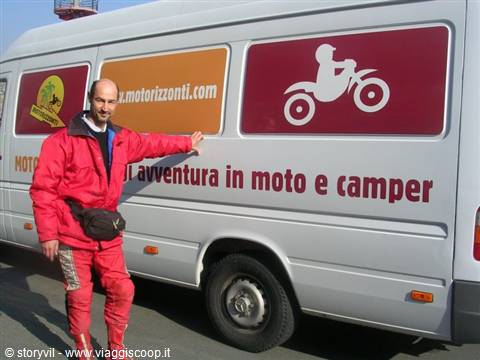 Man in red suit beside a grey camper van with motorcycle advertising