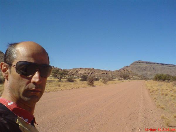 Man in sunglasses on white gravel road among bushes and rocky mountains
