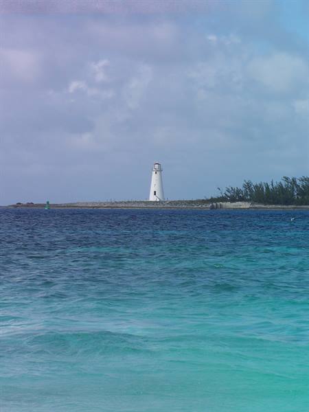 White lighthouse on rocky islet, turquoise sea, cloudy sky at Nassau