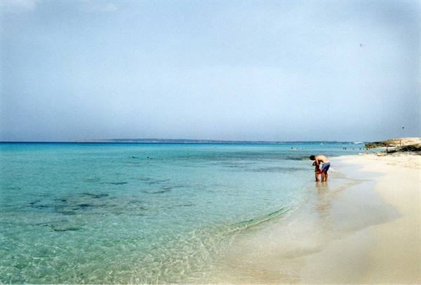 Man knee-deep in clear turquoise water along a white sand beach