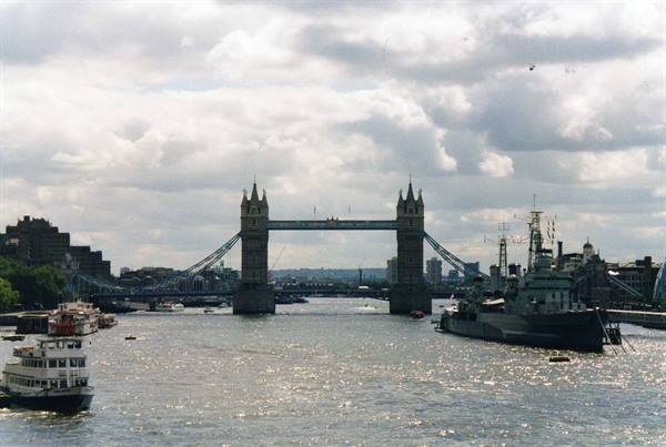 Tower Bridge over the Thames, moored warship and boats, cloudy sky