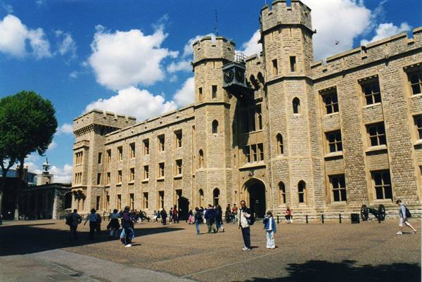 Tourists walk in front of the stone facade of the Tower of London under blue sky