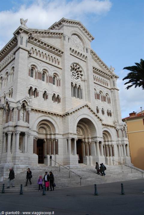 Monaco Cathedral in white stone, tourists walk down the steps under blue sky