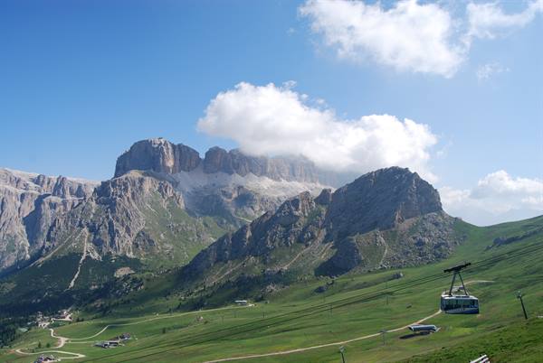 Cable car crosses green meadow beneath the rocky Dolomites cliffs