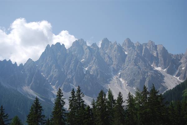Jagged Dolomite peaks above a fir forest, white clouds and blue sky
