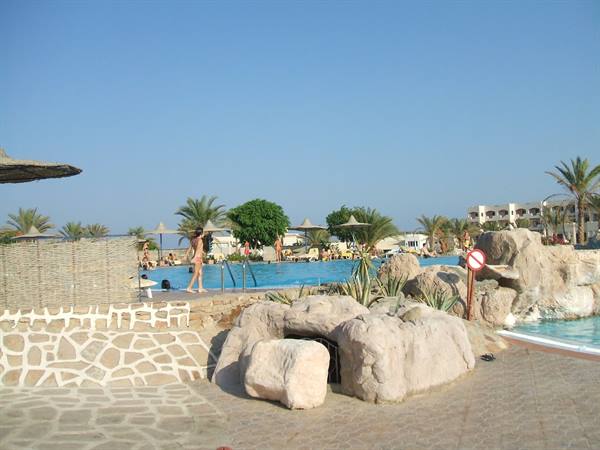 Swimming pool with artificial rocks, palms and parasols, a woman walks on the walkway