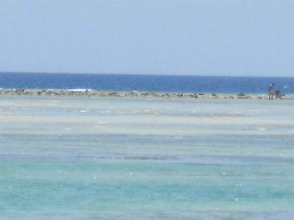 Turquoise shallow water and dark reef, one person standing on the reef