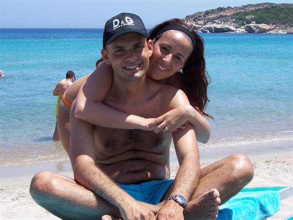 Couple hugging on the sand in front of turquoise sea, she hugs his shoulders