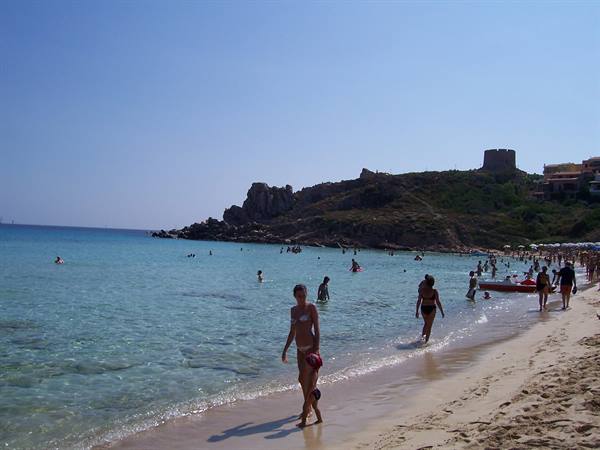 Bathers on the sand in front of a stone coastal tower, turquoise water