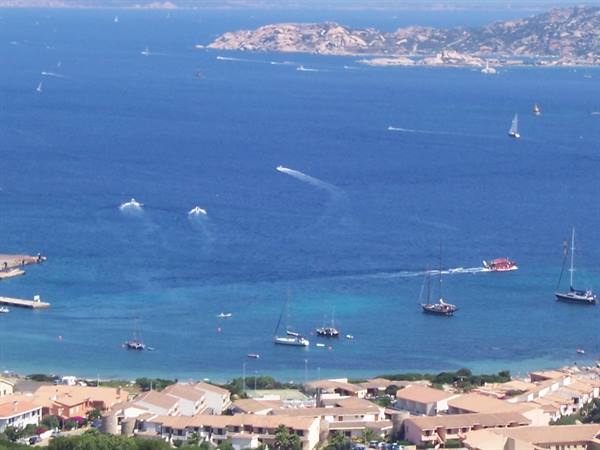Sailboats and motorboats in a turquoise bay above rooftops