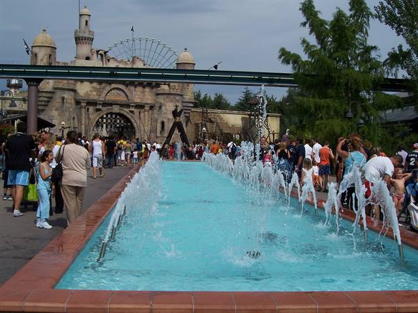 Fountain jets, crowds and a themed castle entrance at an amusement park
