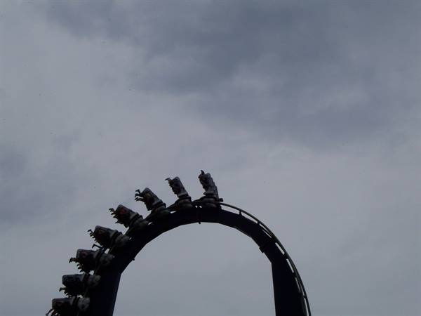 Roller coaster train loops upside down against a cloudy sky
