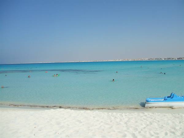blue pedal boat on white sand, swimmers in turquoise shallow water