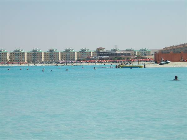 Swimmers in turquoise water in front of a hotel and beach umbrellas