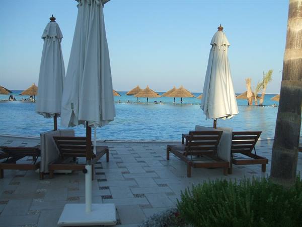 Closed umbrellas and empty loungers by the pool, straw umbrellas by the sea