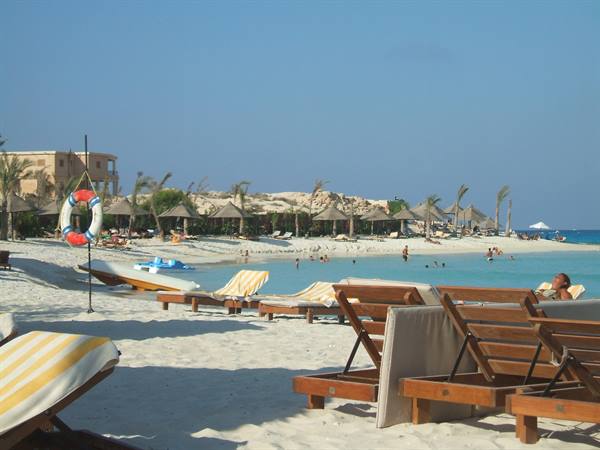 White sand beach with wooden loungers, straw umbrellas and swimmers in turquoise water