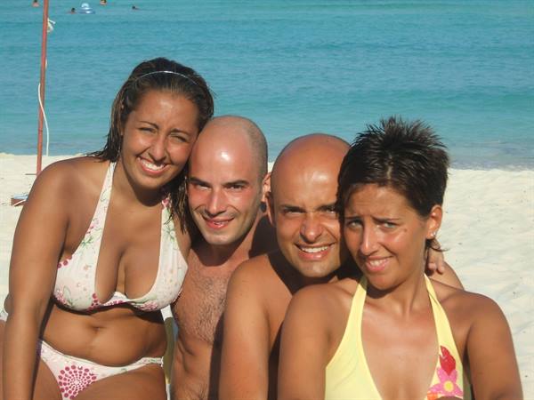 Four friends in swimwear smile together on the white sand beach