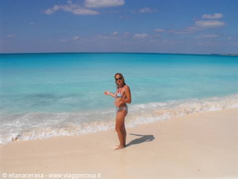Woman in bikini on white sand before turquoise sea and blue sky