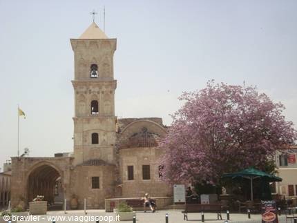 Stone bell tower of Saint Lazarus in Larnaca with blooming jacaranda tree