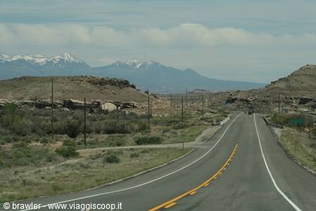Straight road through desert shrubs with snowy mountains in the distance