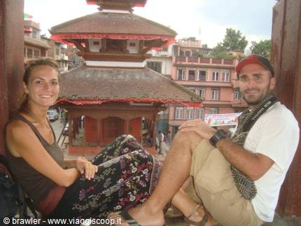 Two tourists sitting on a wooden terrace in front of a brick temple in Kathmandu