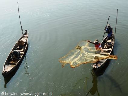 Fishermen on wooden canoes throwing yellow nets over green water