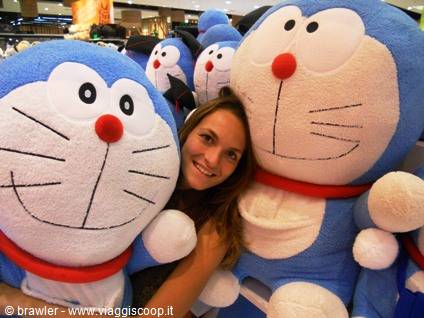 Smiling girl posing among large Doraemon plush toys in a mall