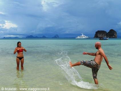 Man and woman splashing in turquoise water near yacht and limestone cliffs